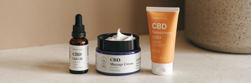 Table avec des produits CBD : bouteille d'huile CBD, crème de massage CBD et crème solaire au CBD, sur fond beige.