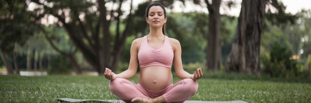 Photographie d'une femme enceinte pratiquant du yoga prénatal dans un environnement paisible, mettant en lumière des solutions naturelles et sans risque pour les inconforts durant la grossesse.