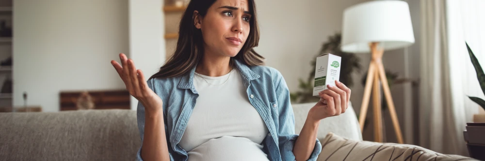 Image représentant une femme enceinte hésitante, tenant une boîte de CBD dans ses mains, symbolisant le doute et les questions liées à l'utilisation de cette substance pendant la grossesse.